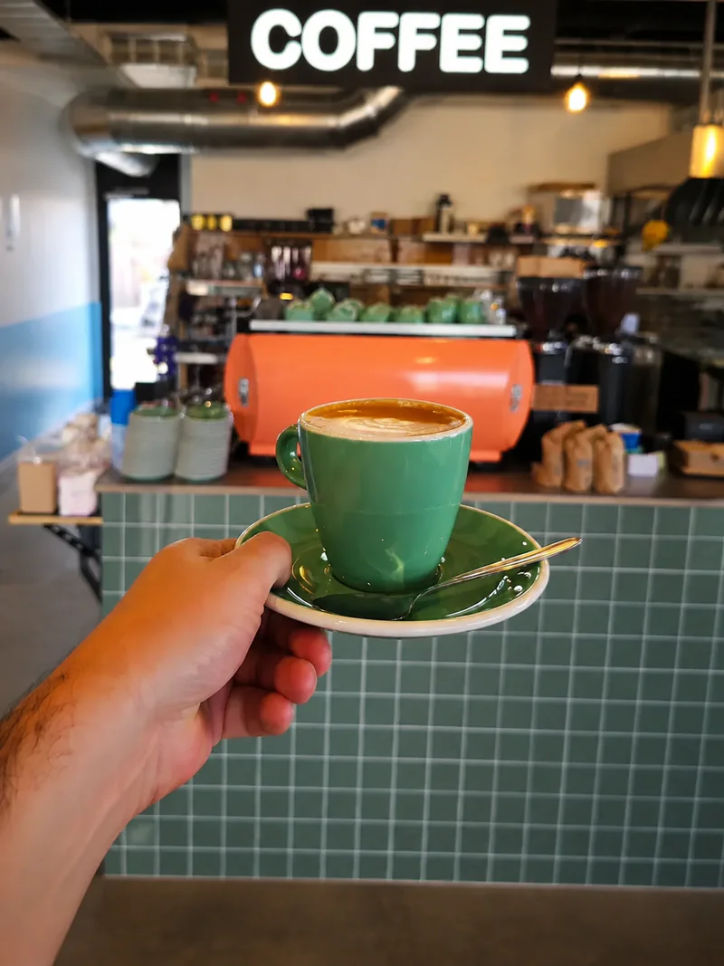 A green coffee cup held in front of Yellow’s coffee counter