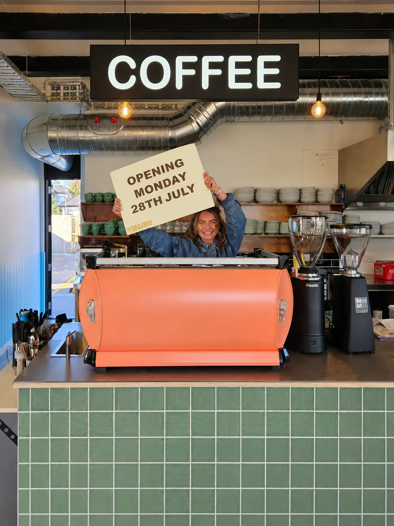 Orange espresso machine beneath a COFFEE sign inside Yellow Cafe and Roastery